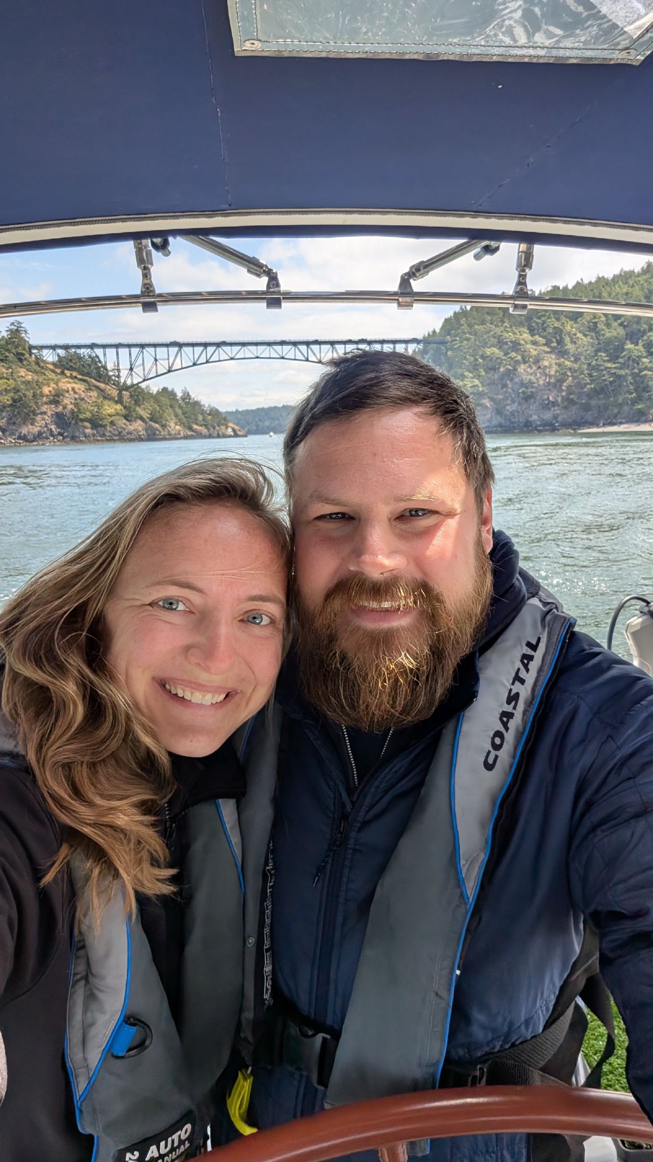Rachel and Brian taking a selfie while sailing through Deception Pass with the bridge behind them