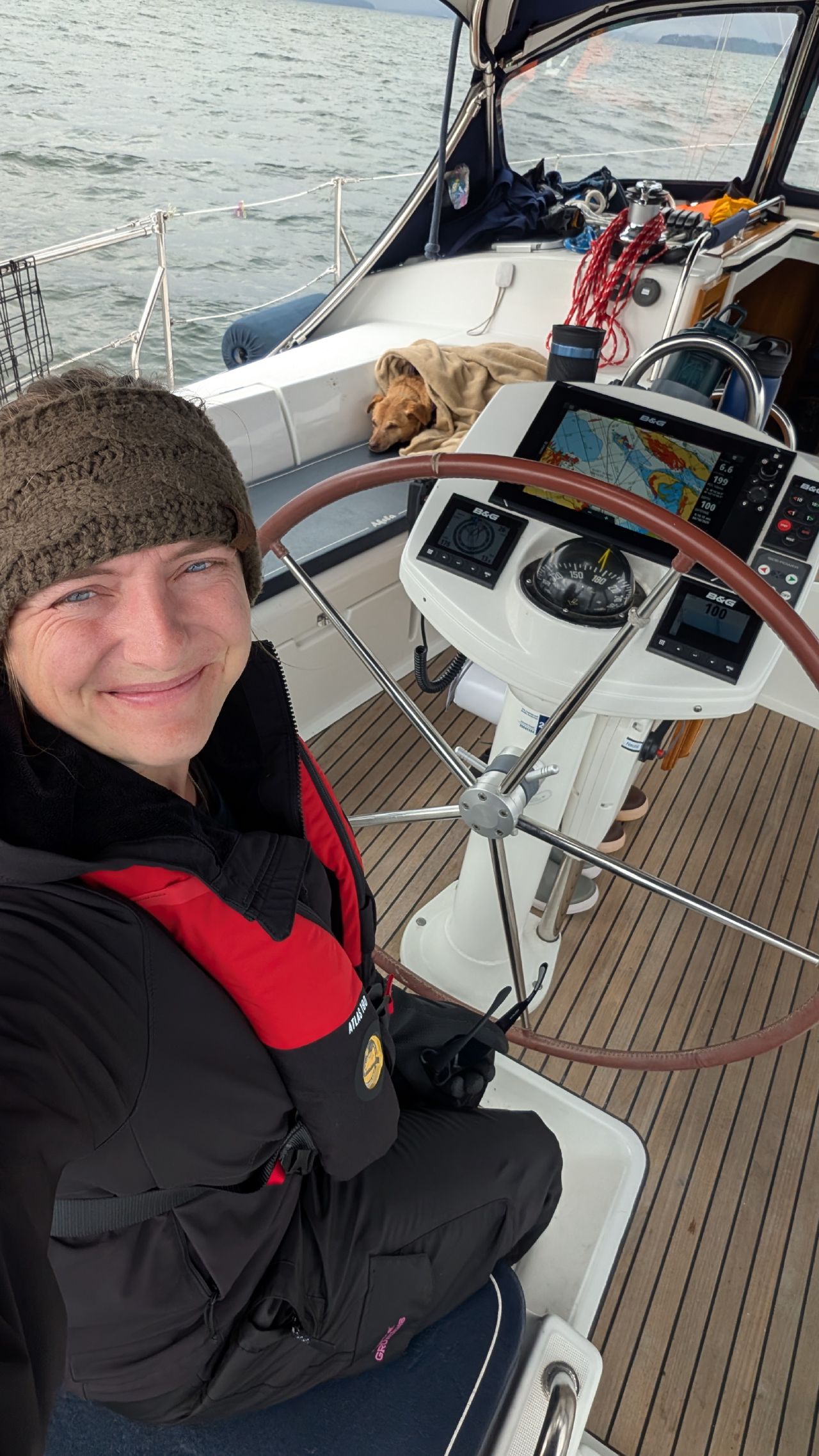 Rachel at the helm in rainy weather with Maui sleeping behind and the chartplotter showing the route