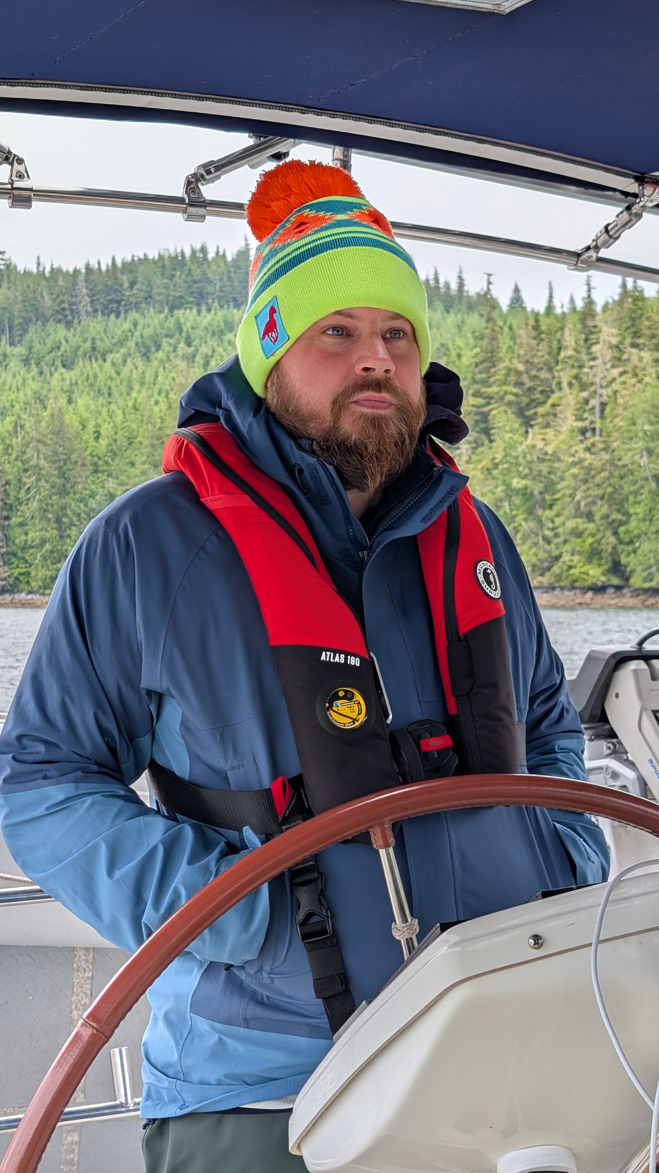 Brian focused at the helm in a colorful beanie and life jacket navigating Johnstone Strait