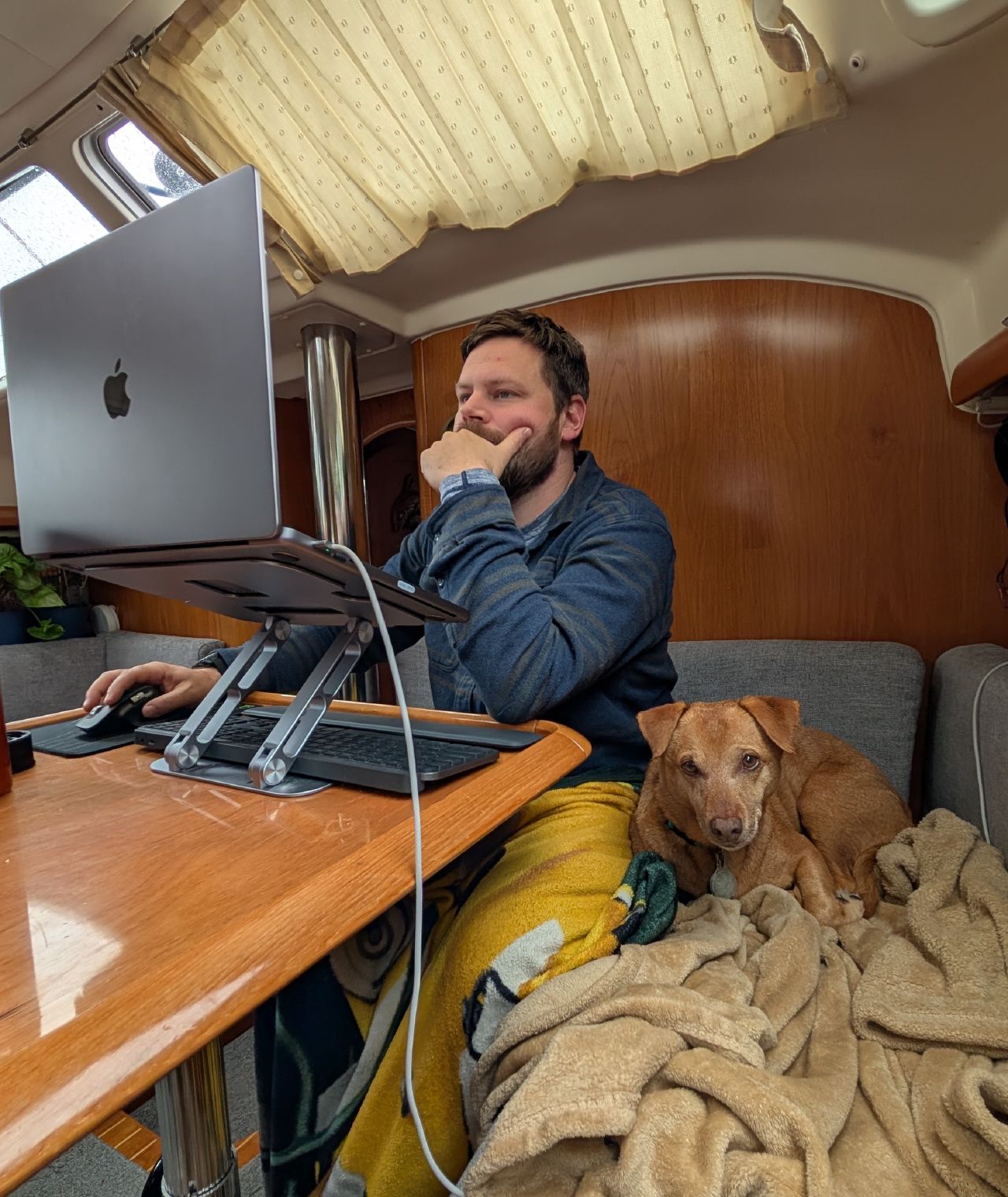 Brian working on his laptop with Maui curled up beside him below deck on SV Yahara