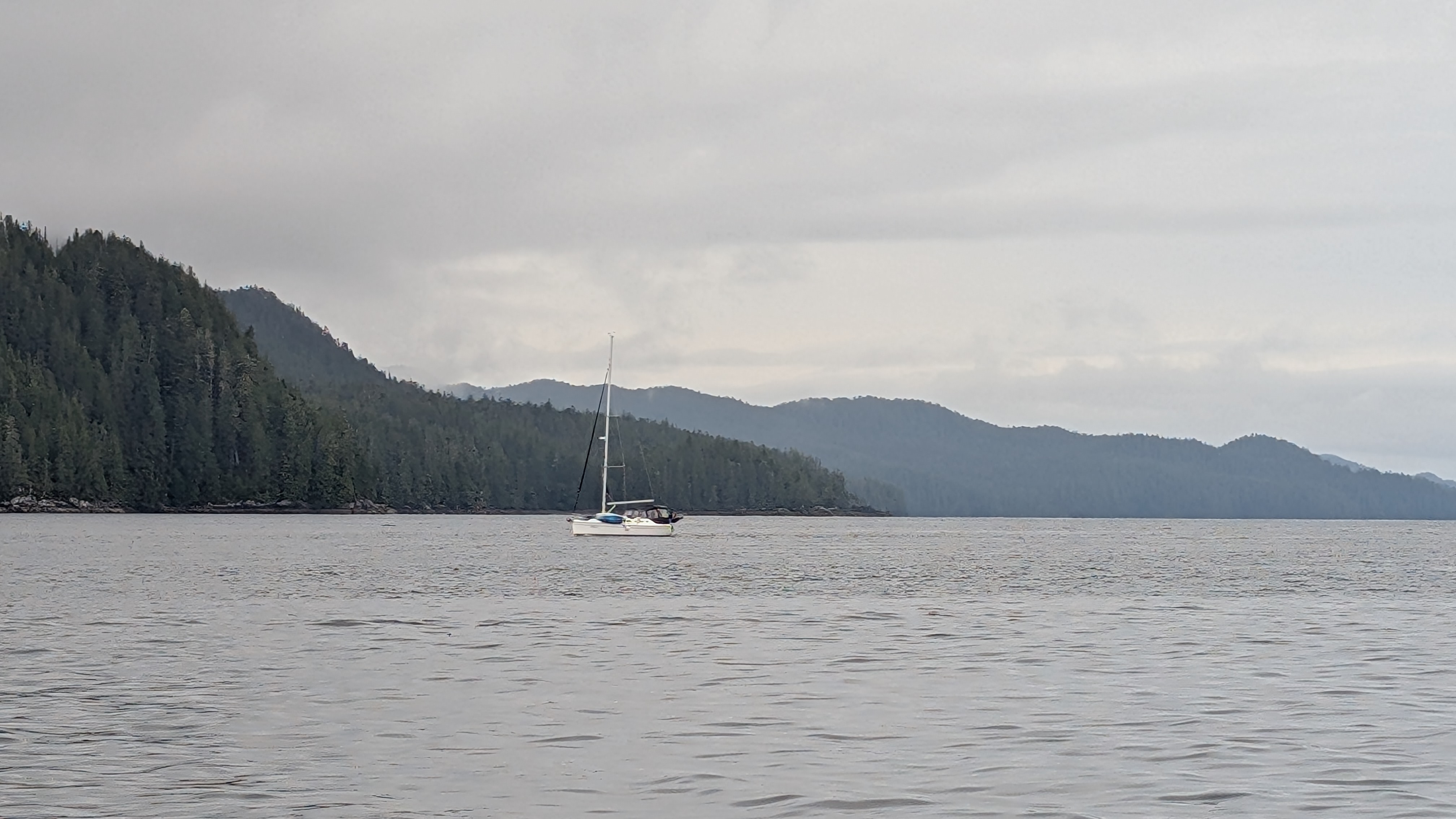 A lone sailboat anchored with misty forested mountains in the background
