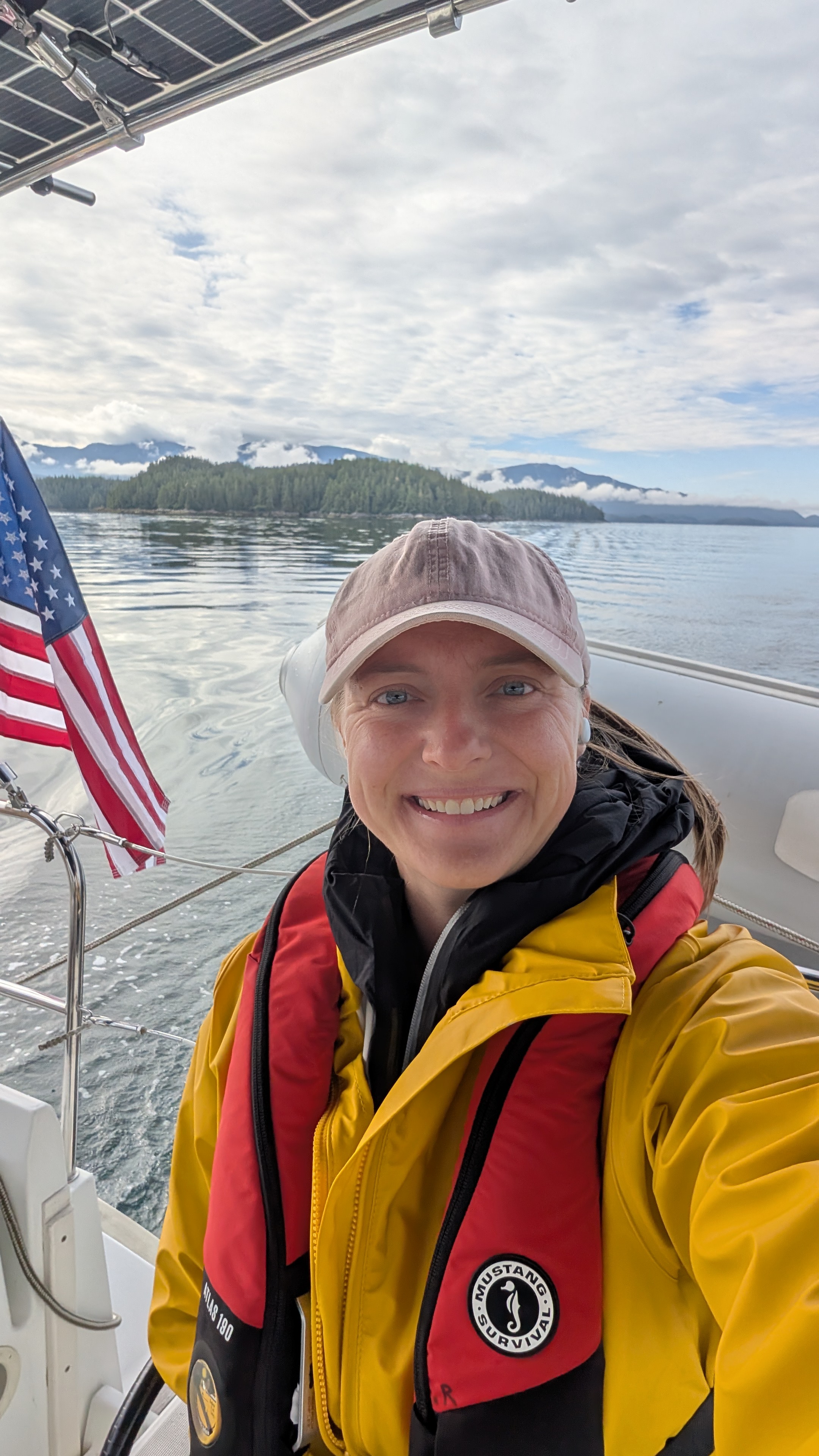 Rachel smiling in her life jacket and foul weather gear at the helm on the passage to Codville