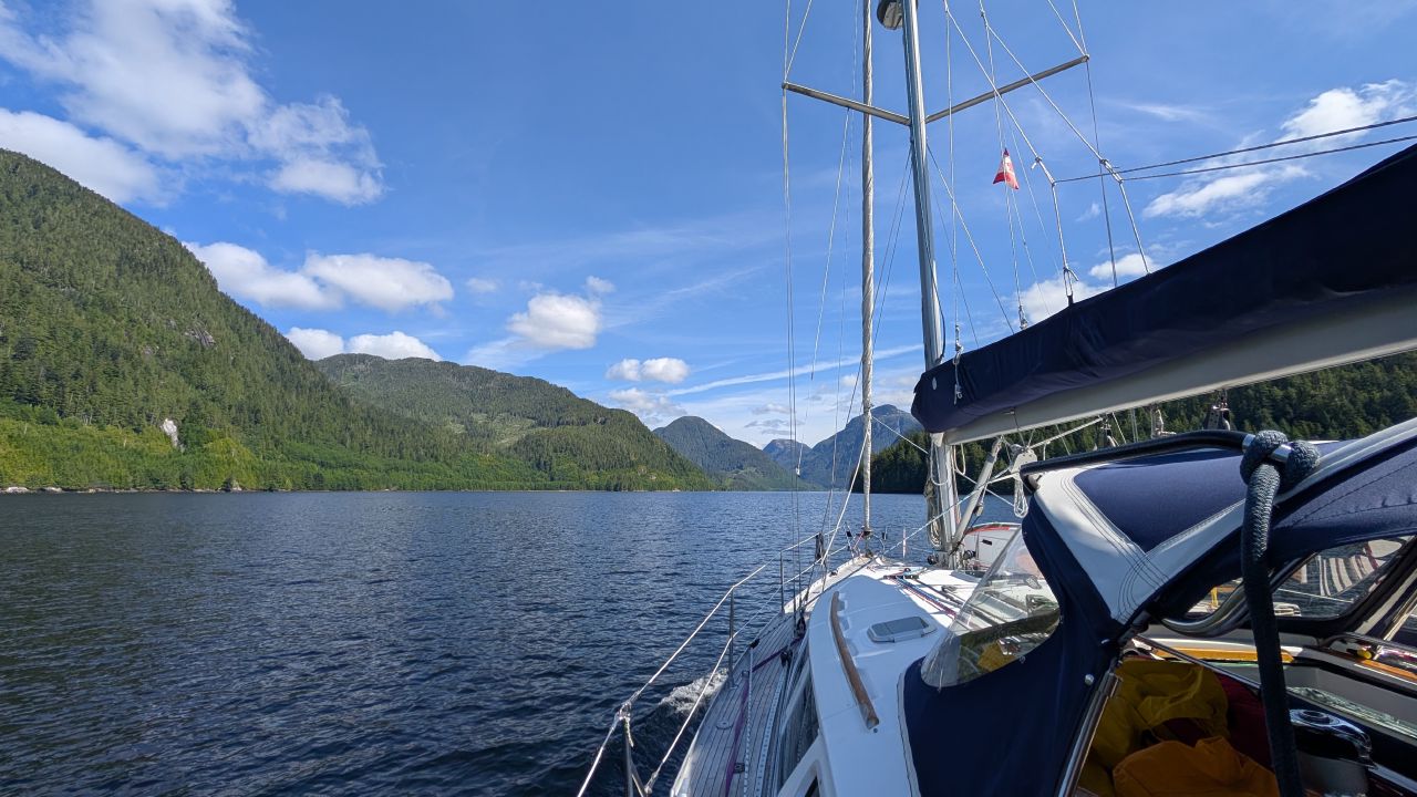View from the foredeck of SV Yahara sailing into the sunny inlet approaching Ocean Falls
