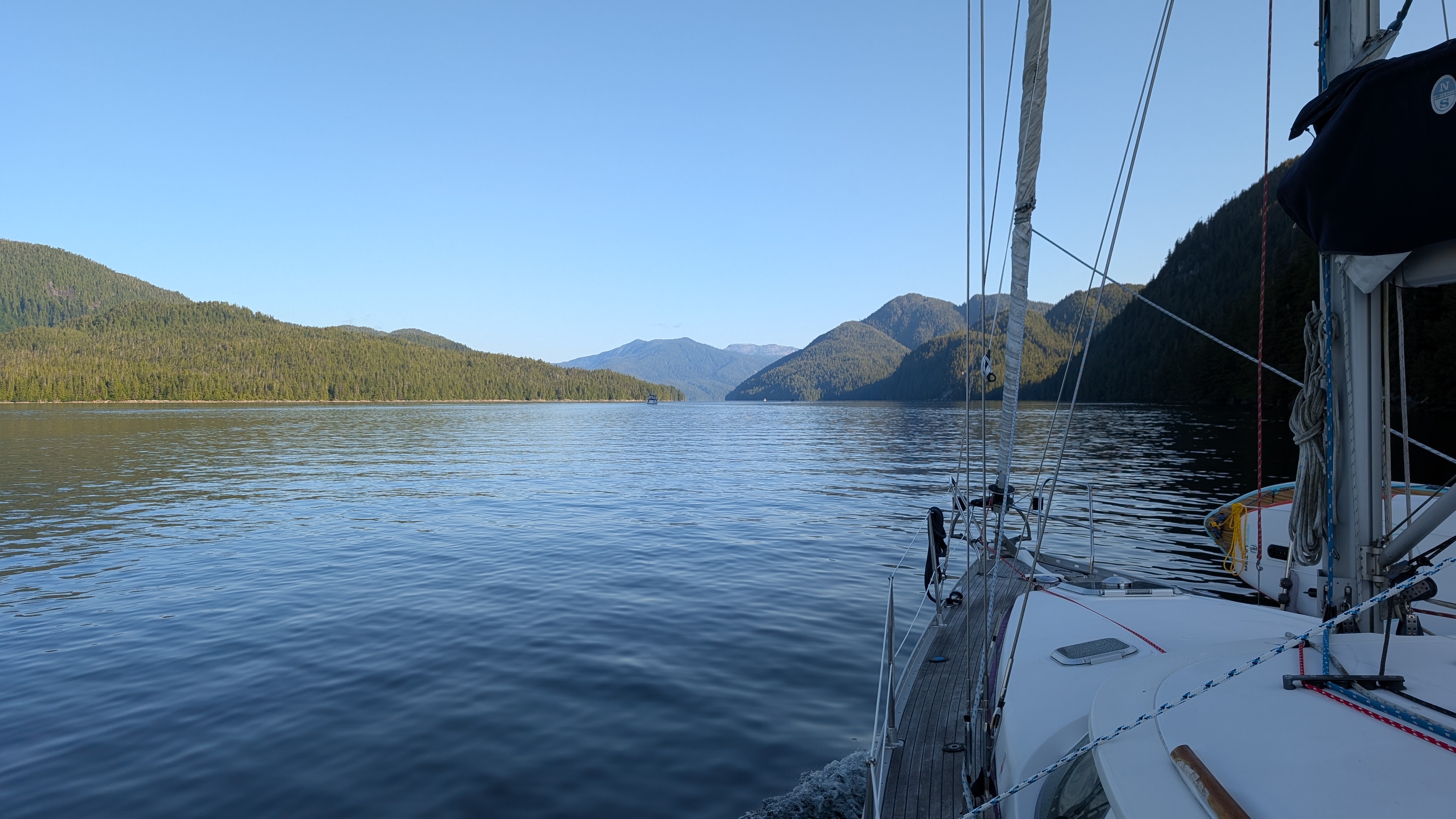 View from the deck of SV Yahara motoring through a glassy channel flanked by forested mountains
