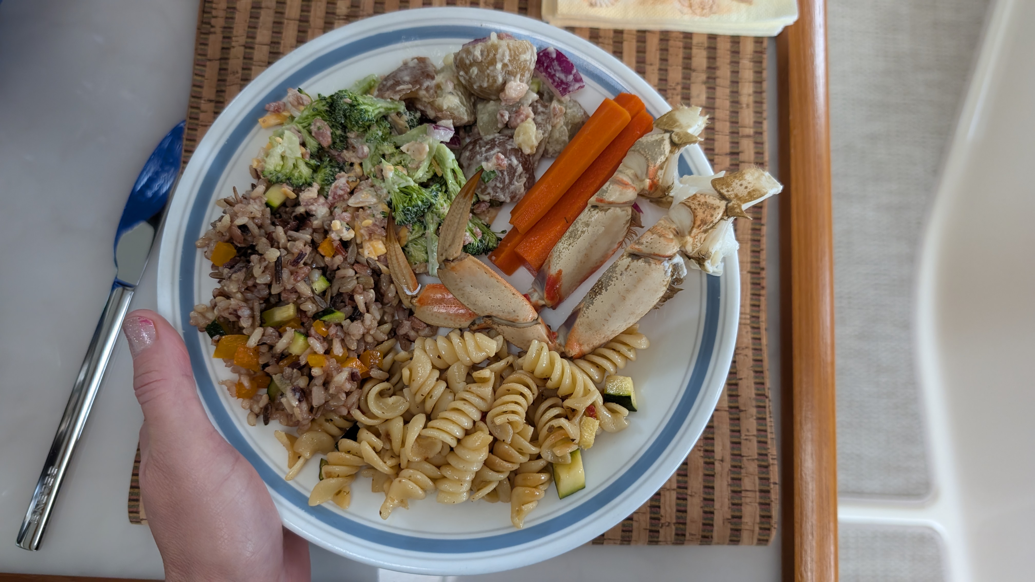 Potluck lunch plate loaded with crab legs, pasta salad, wild rice, broccoli salad, and potato salad