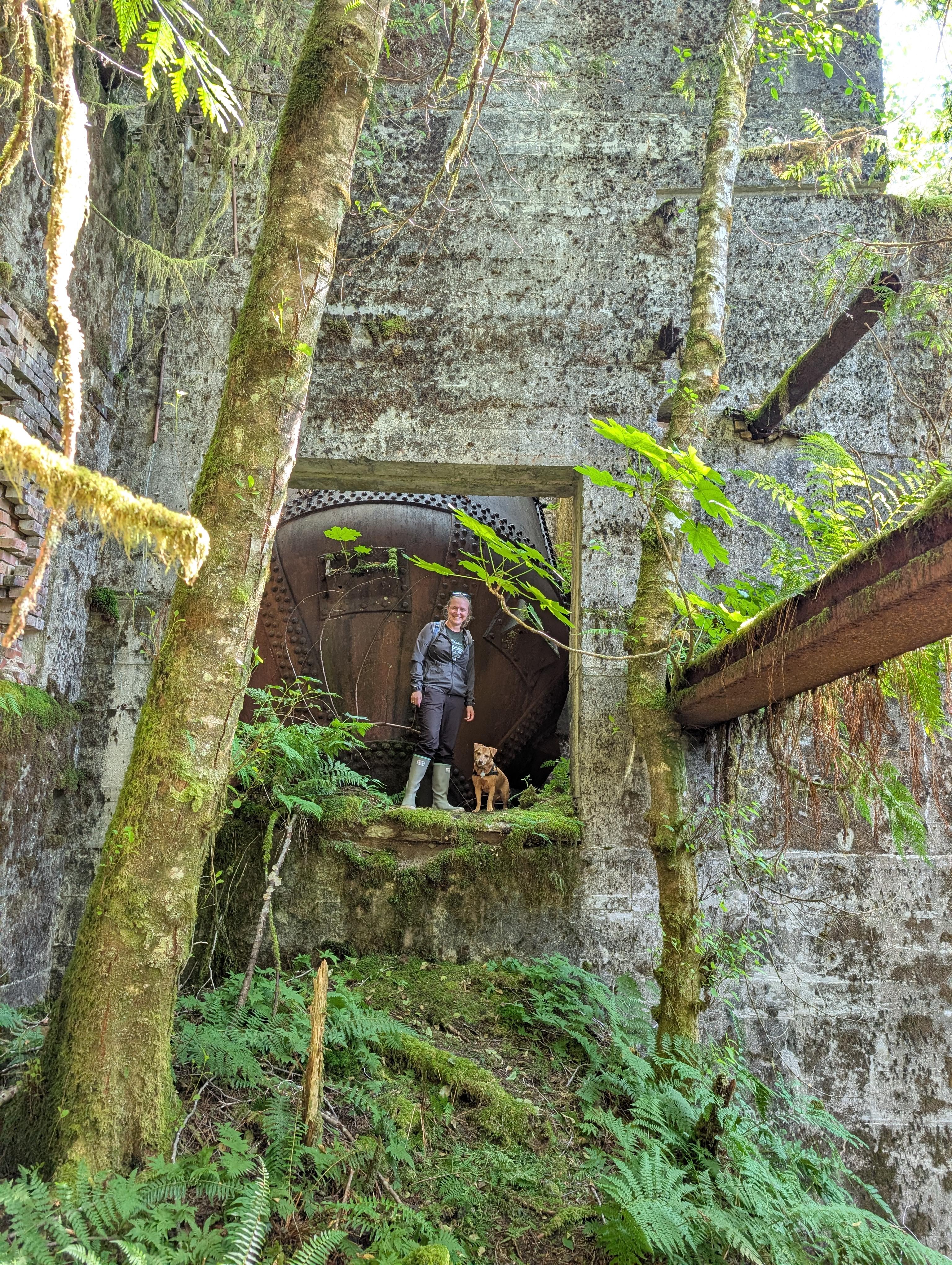 Rachel and Maui standing in a doorway of the overgrown concrete ruins with a large rusted boiler behind them