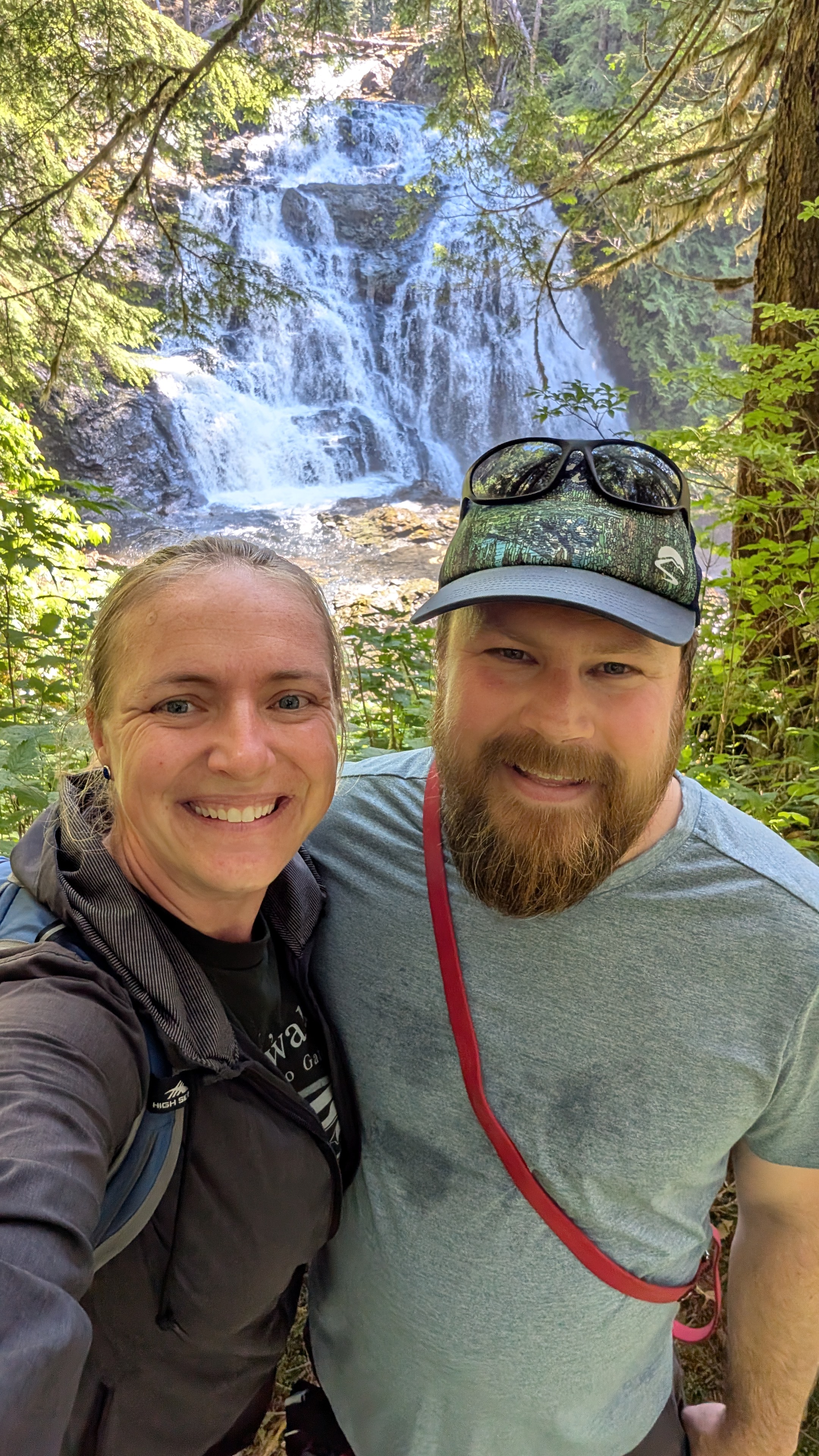 Rachel and Brian smiling for a selfie with a beautiful multi-tiered waterfall at Swanson Bay