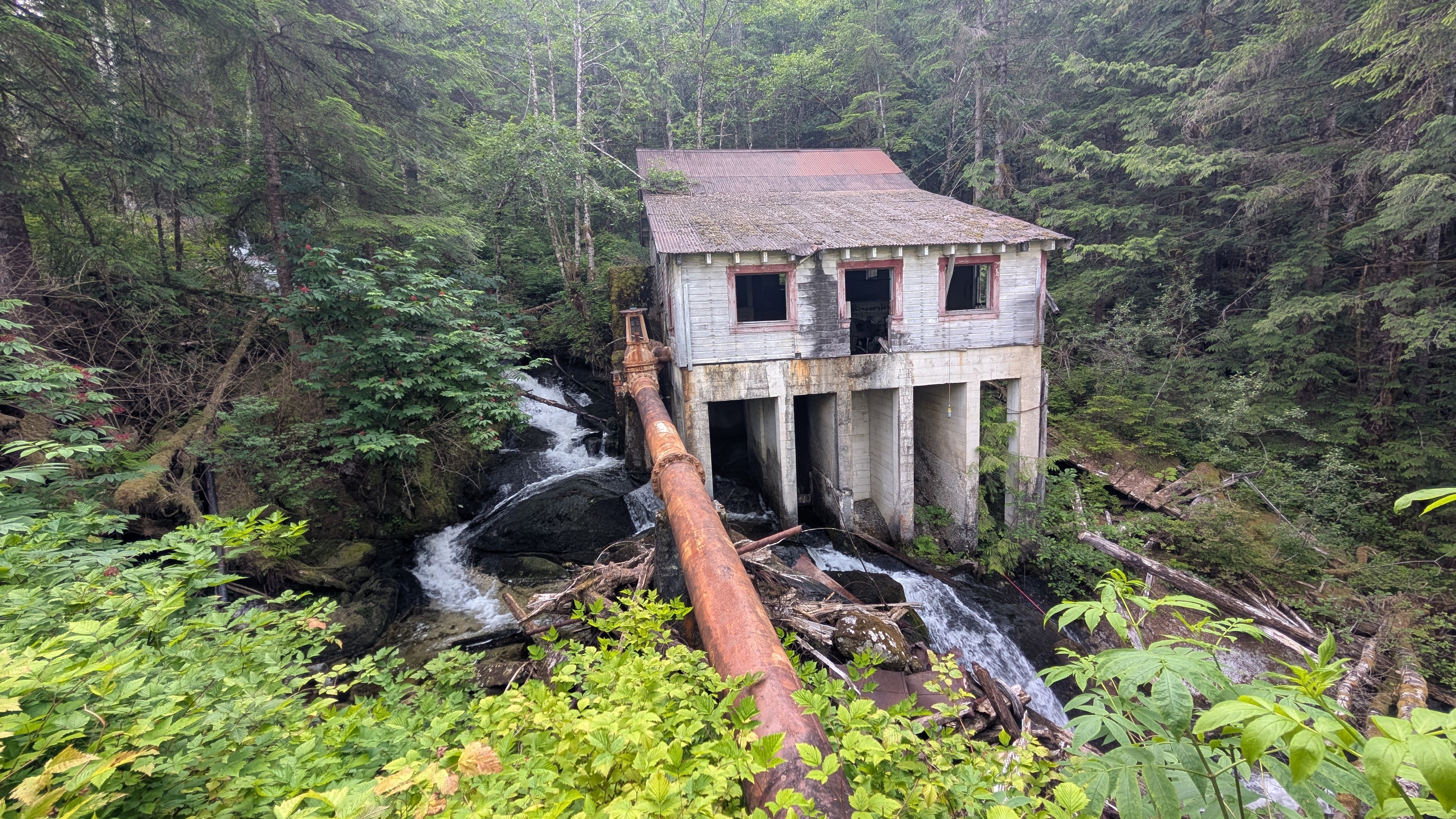 Abandoned concrete powerhouse building with a rusted pipe straddling a waterfall in the Butedale rainforest