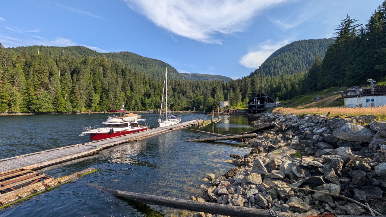 Boats docked at the Butedale cannery site with forested mountains and old buildings on a sunny day