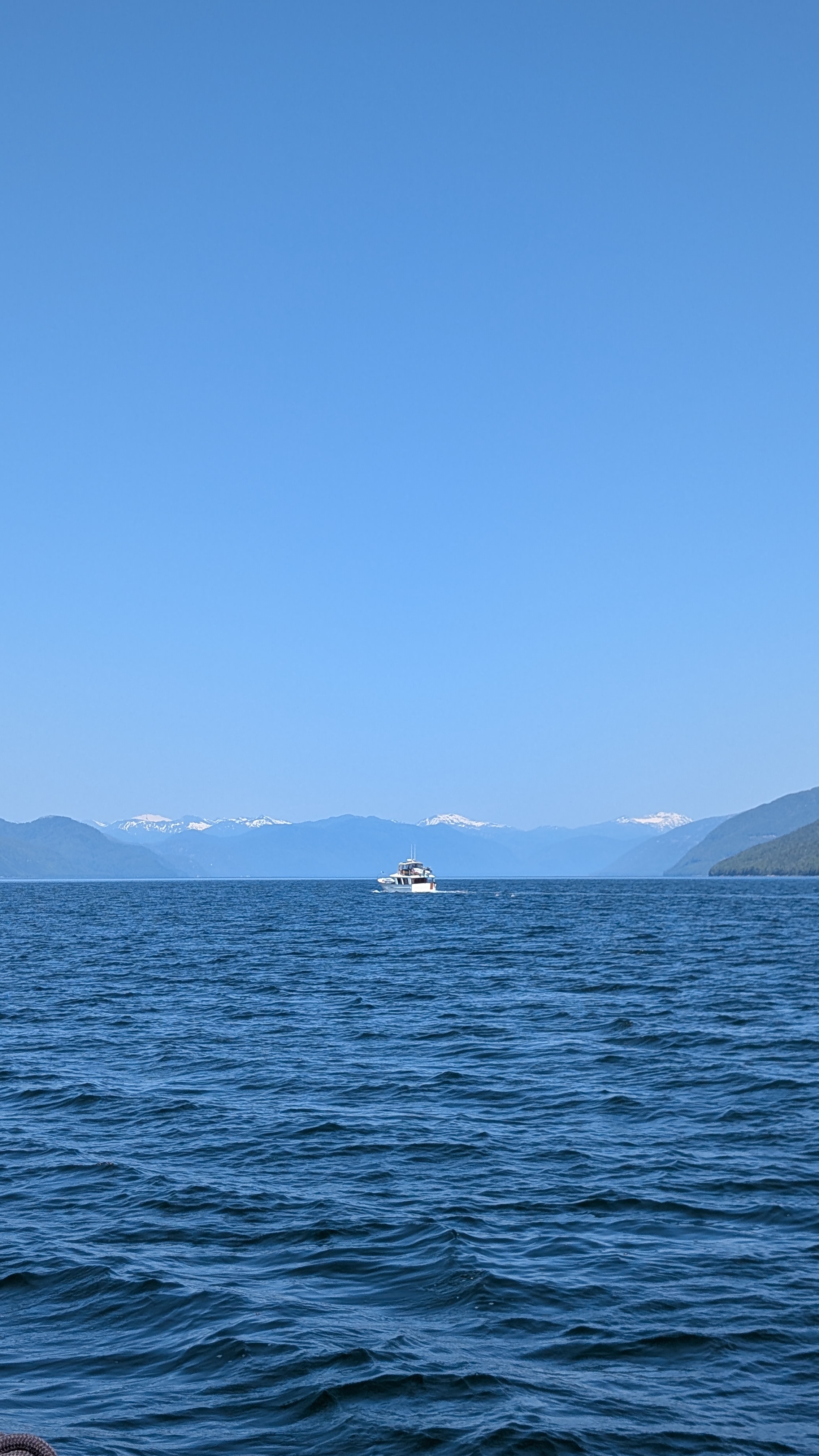 Distant boat on open blue water with snow-capped mountains along the horizon