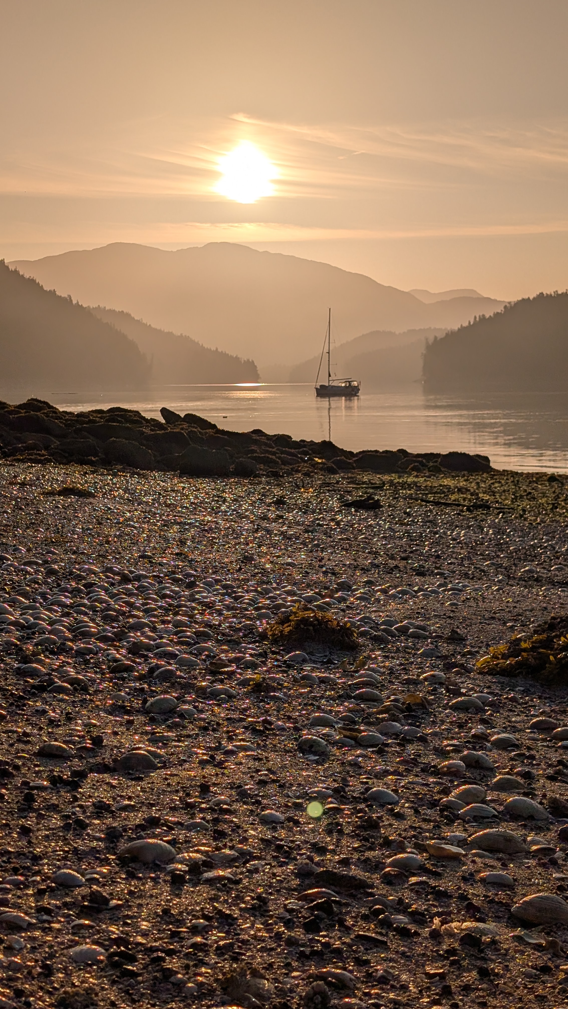 Pebble beach at low tide with a sailboat silhouetted against a golden sunrise
