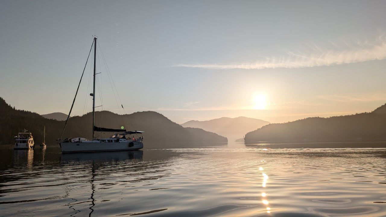 Sailboat anchored in golden sunrise light at Otter Shoal with mountains in the background