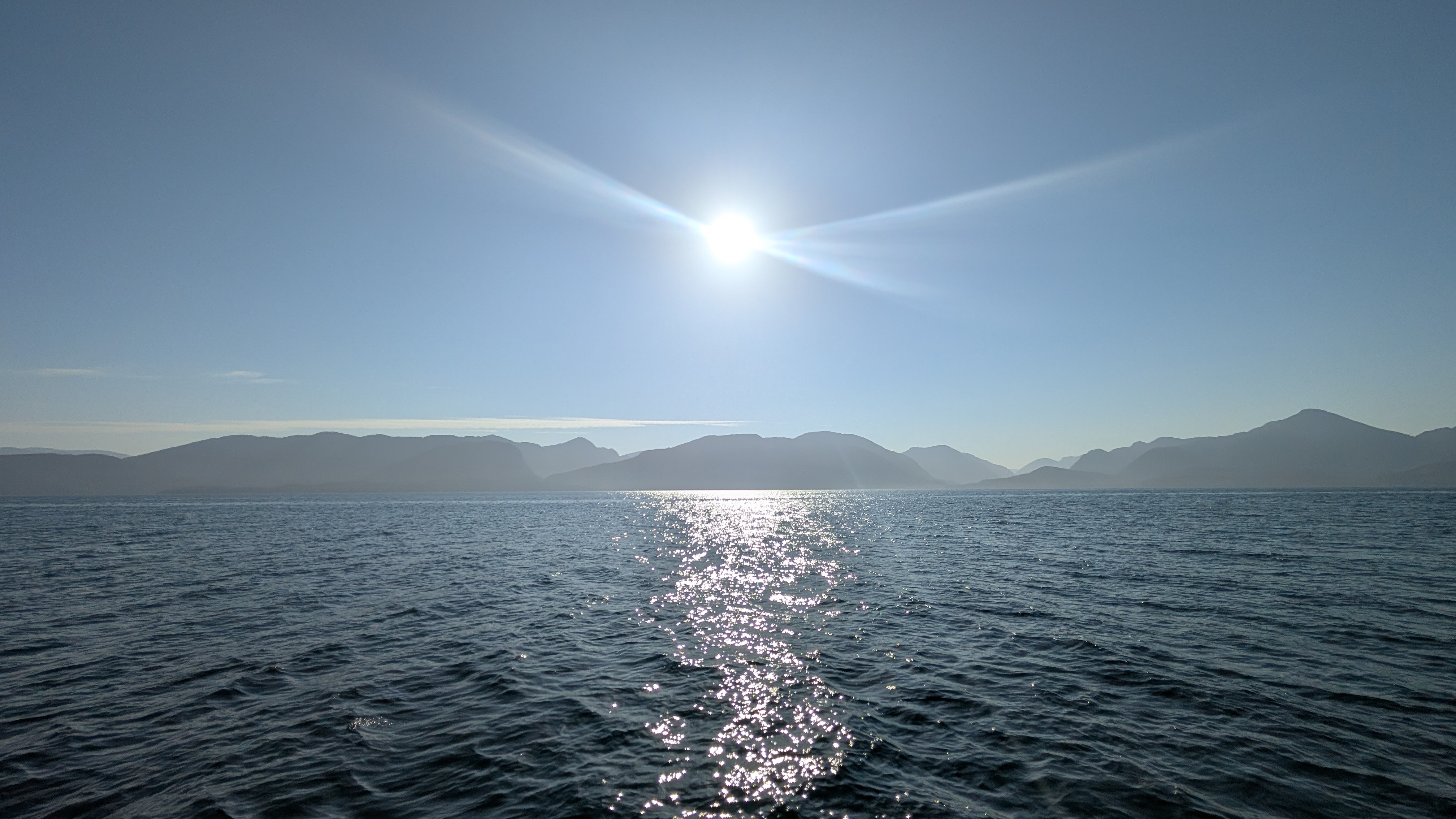 Sun sparkling on open water with mountain silhouettes on the horizon