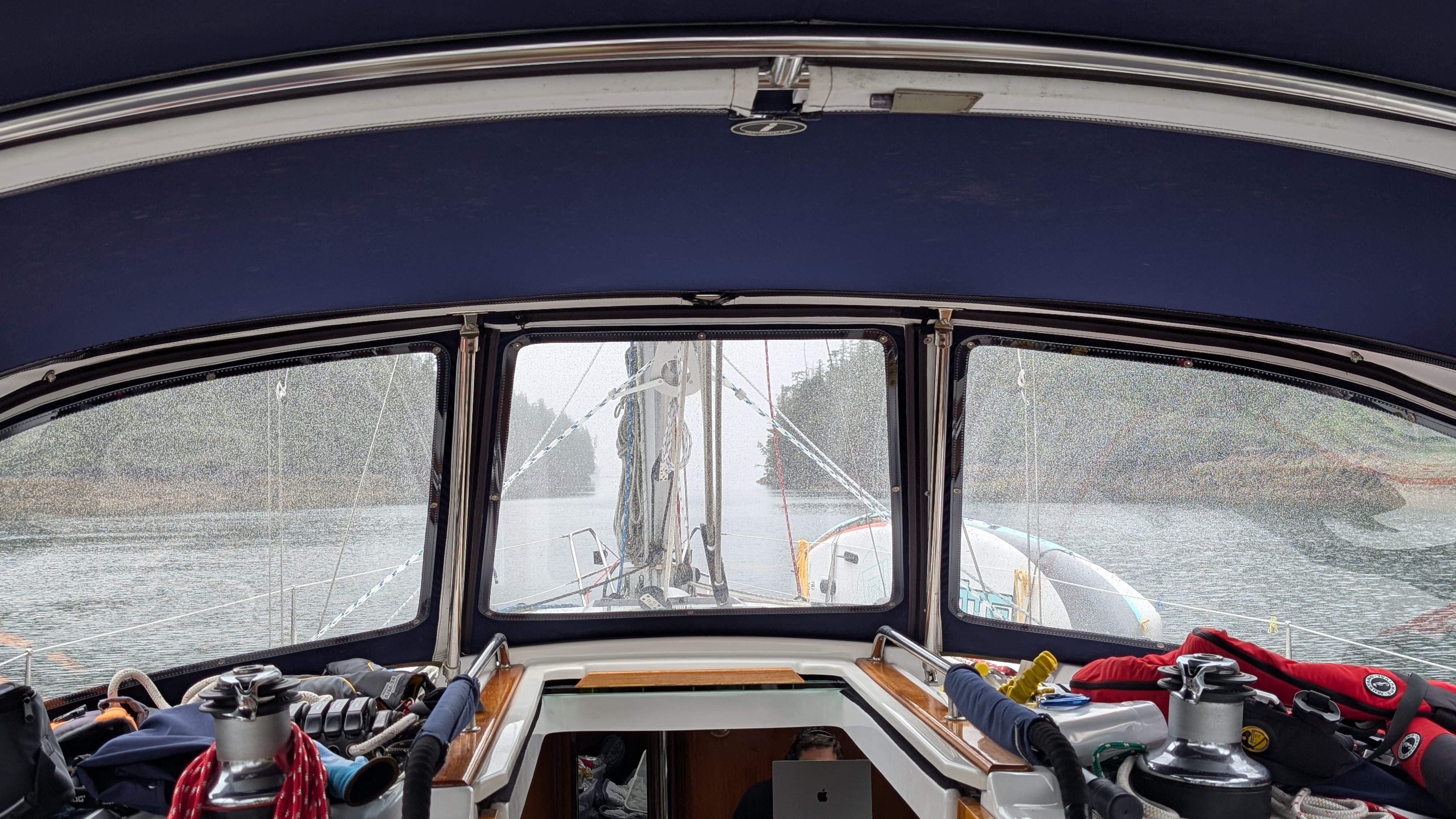 View through rain-splattered dodger windows approaching a narrow pass in the fog