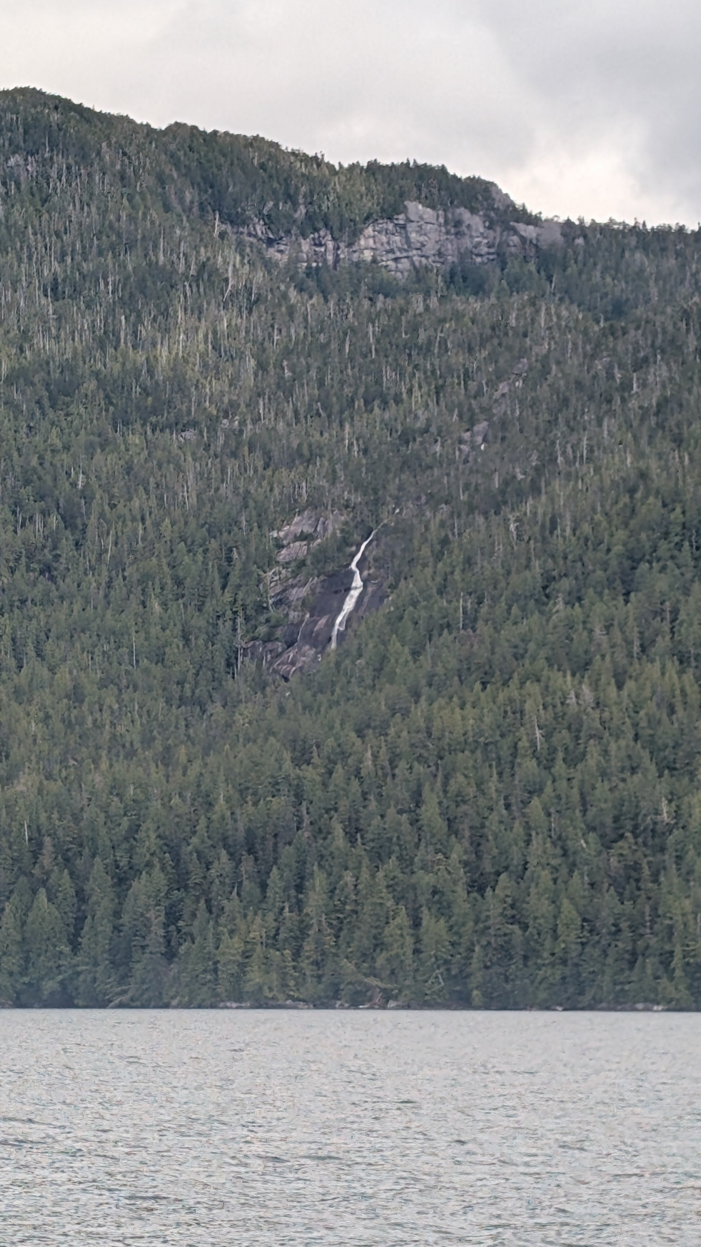 Distant waterfall cascading down a forested mountainside viewed from the water