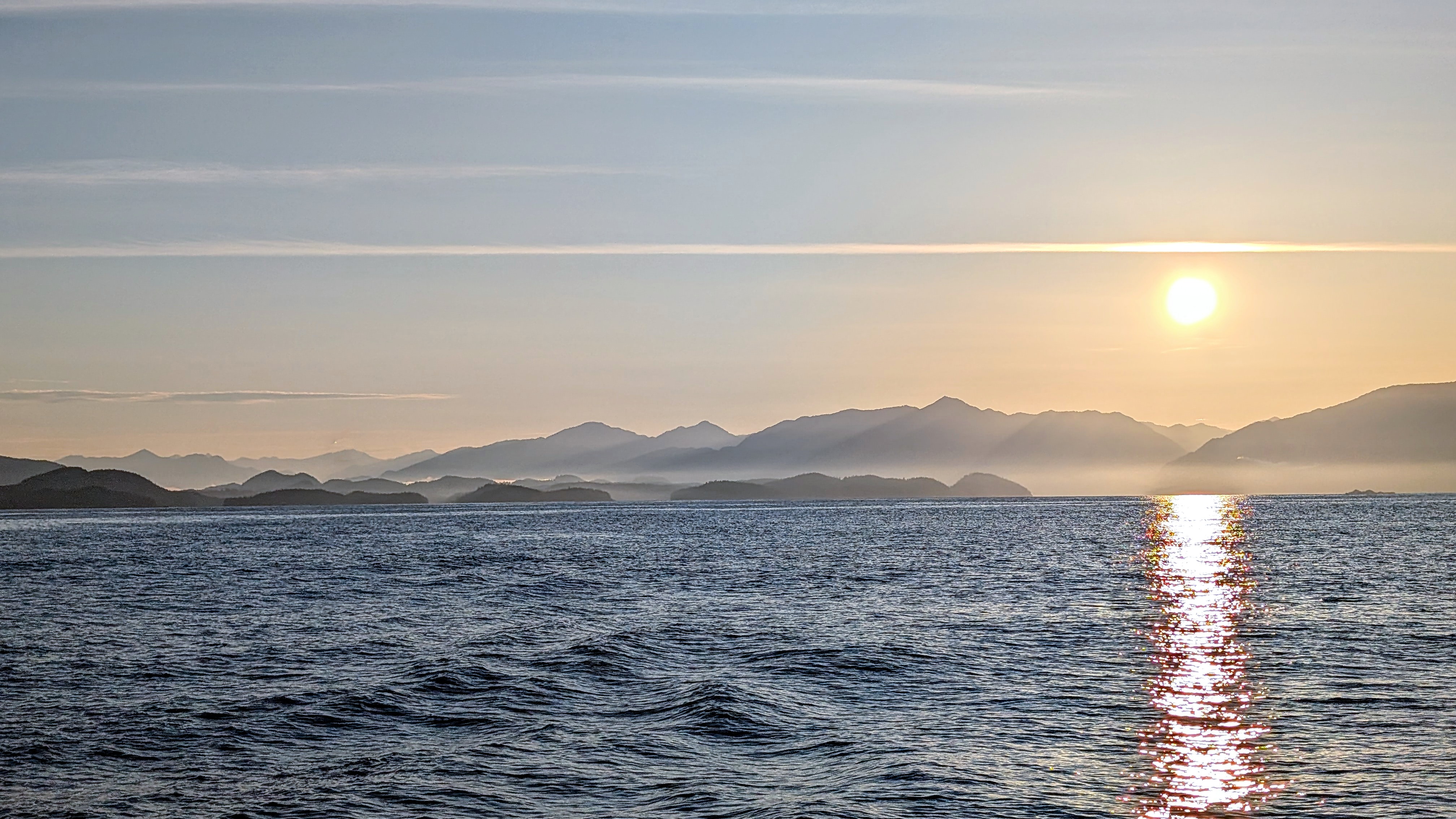 Sunrise over layered misty mountains as SV Yahara leaves the Central Coast heading south around Cape Caution
