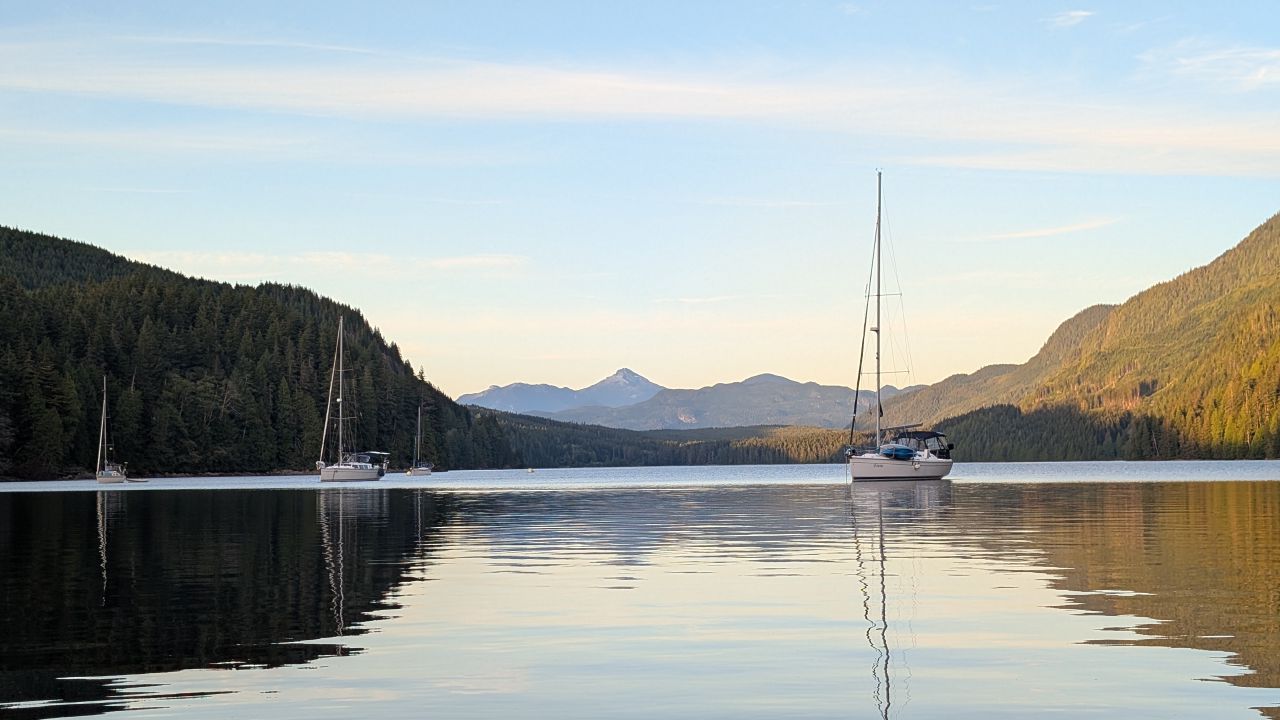 Sailboats anchored in Forward Harbour at sunset with snow-capped mountains reflected in glassy water