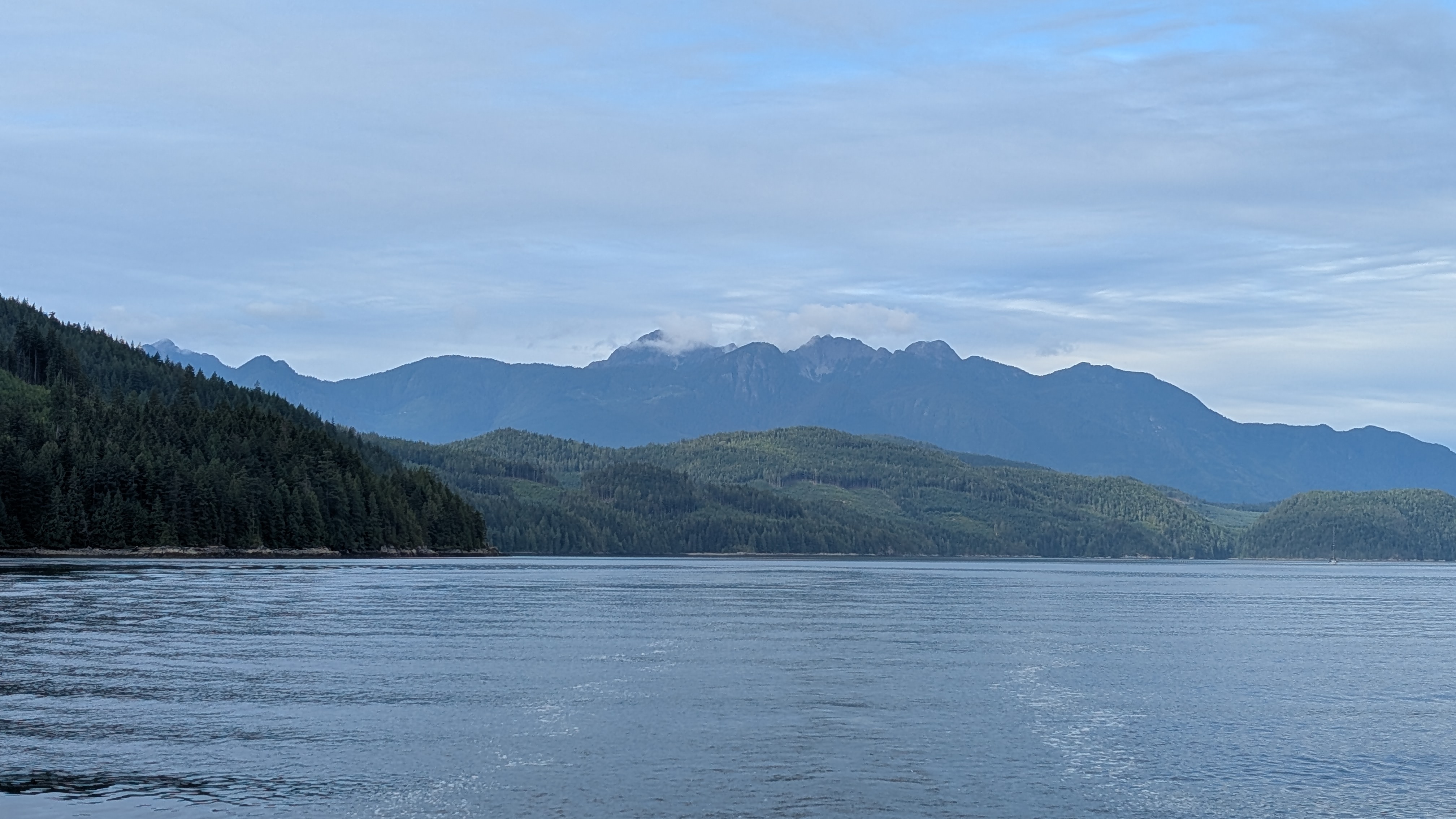 Layered mountains and forested coastline near Green Point Rapids with clouds hovering over the peaks