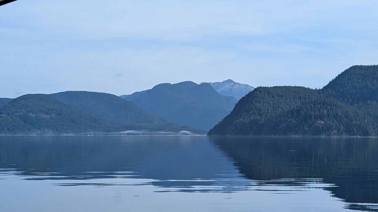 Calm glassy water with layered blue mountains and forested islands during the passage to Octopus Islands