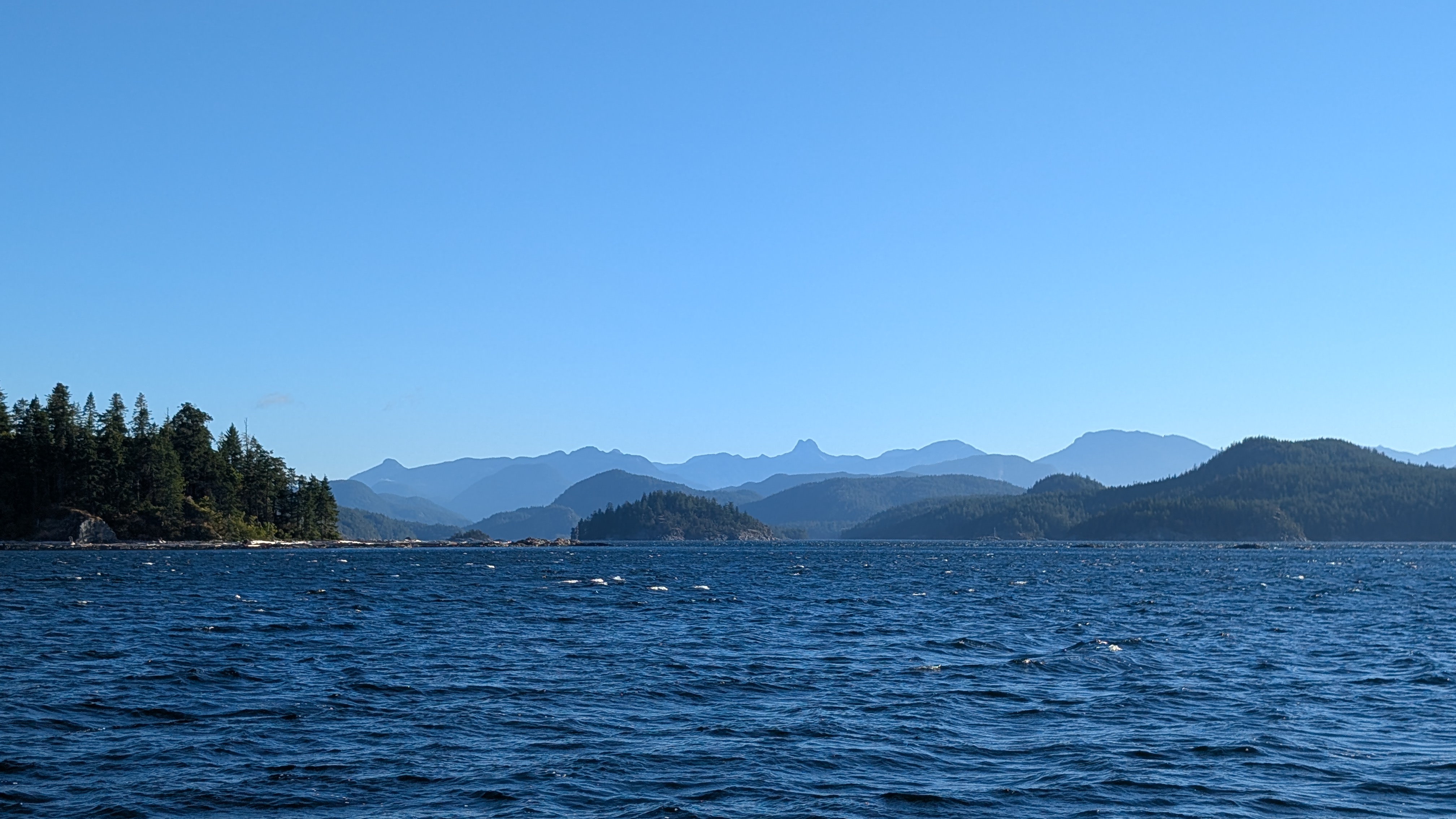 Windy blue water with whitecaps and layered mountain silhouettes approaching Heriot Bay