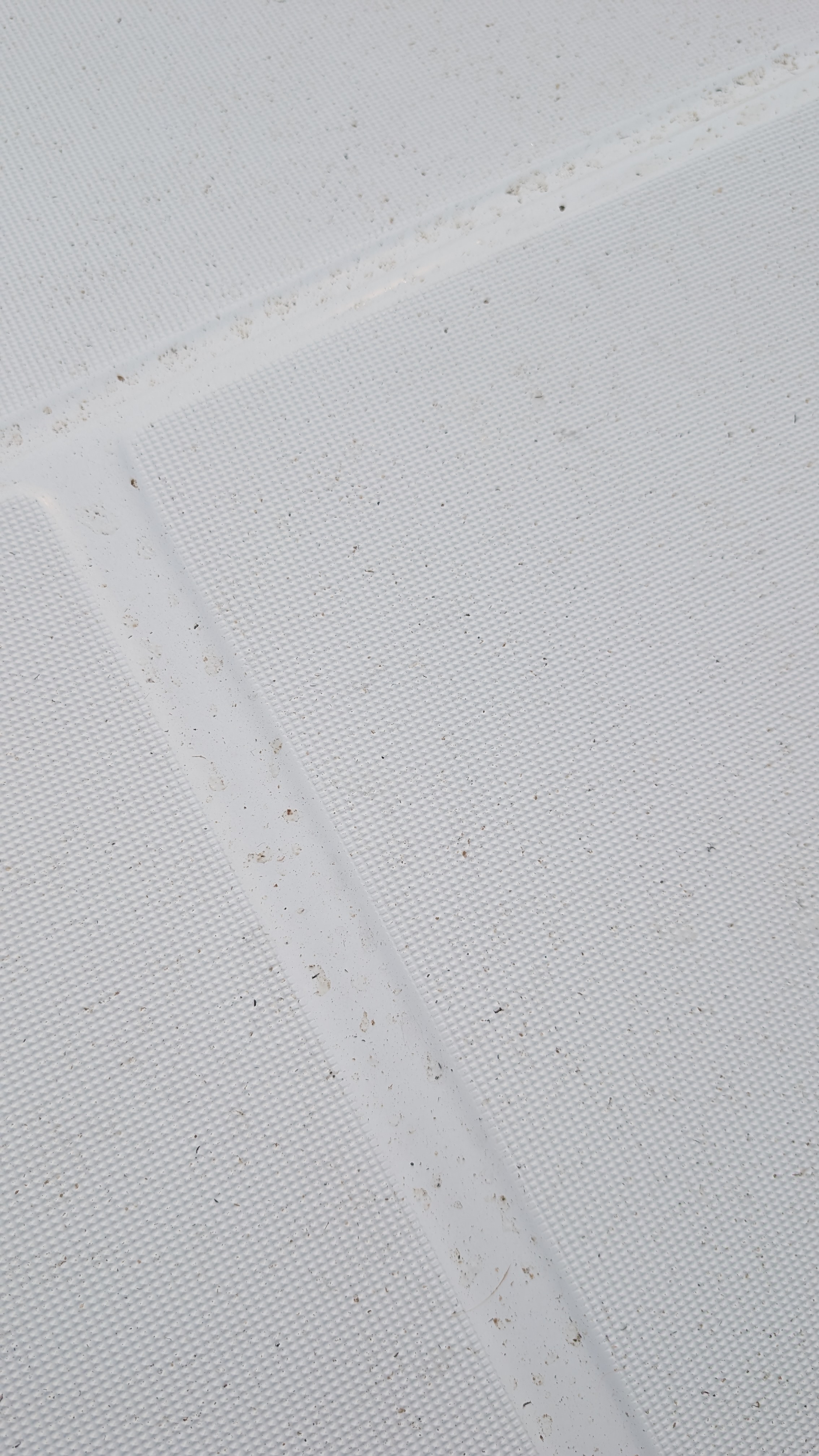 Close-up of wildfire ash particles settled on the white sail cover of SV Yahara