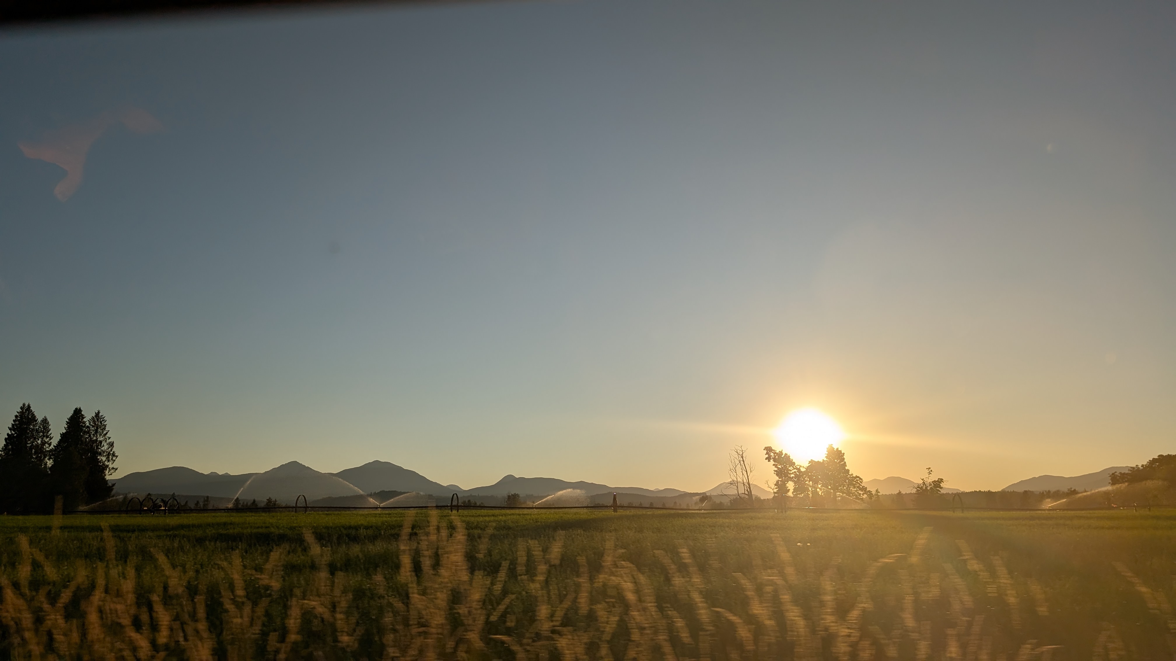 Golden sunset over farmland with irrigation sprinklers and mountains silhouetted in the distance near Ladysmith