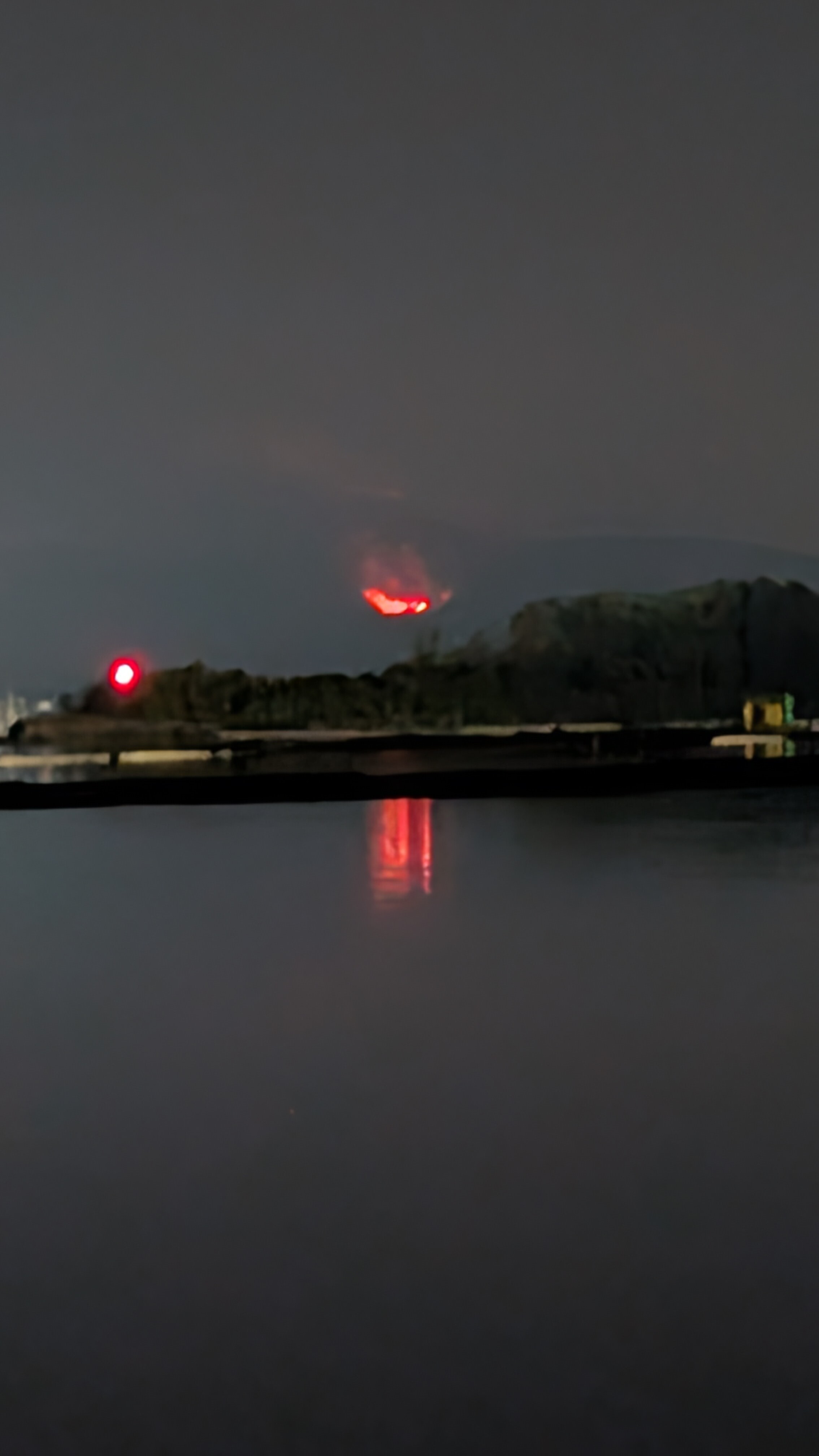 Wildfire burning on a hillside at night with flames reflected in the still water of Ladysmith Harbour