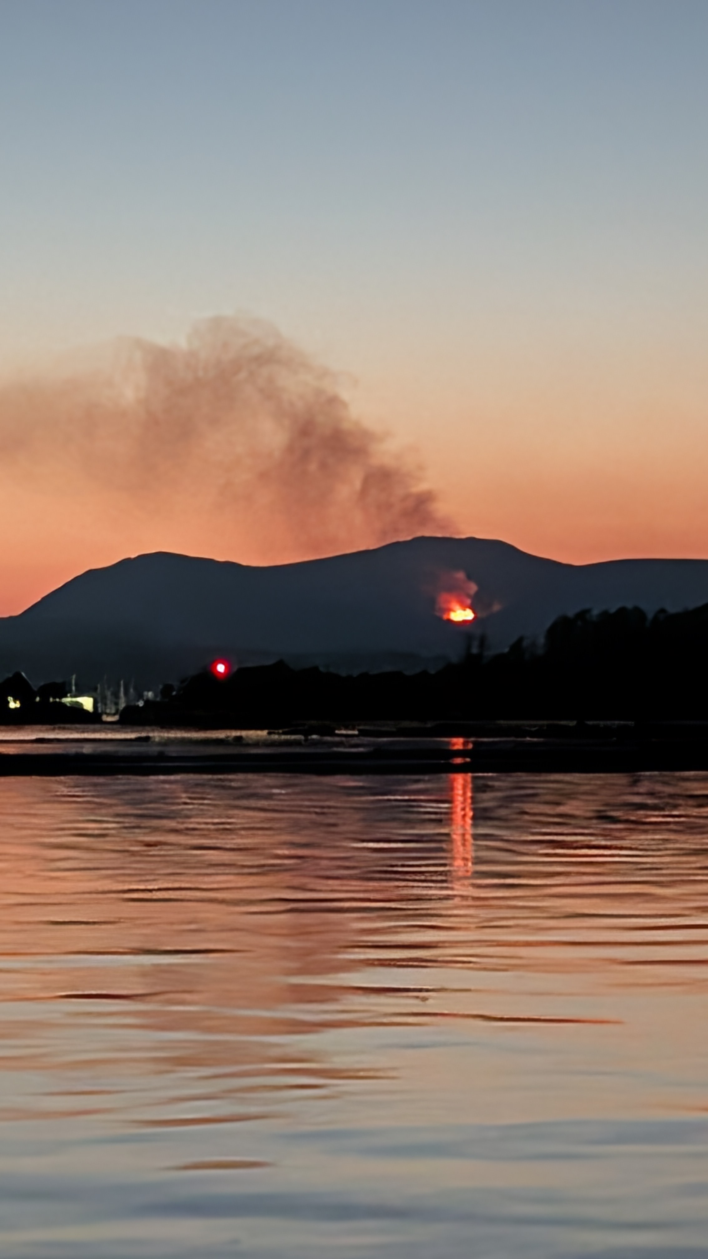 Wildfire glowing orange on a distant mountain with smoke rising into the sunset sky over Ladysmith Harbour