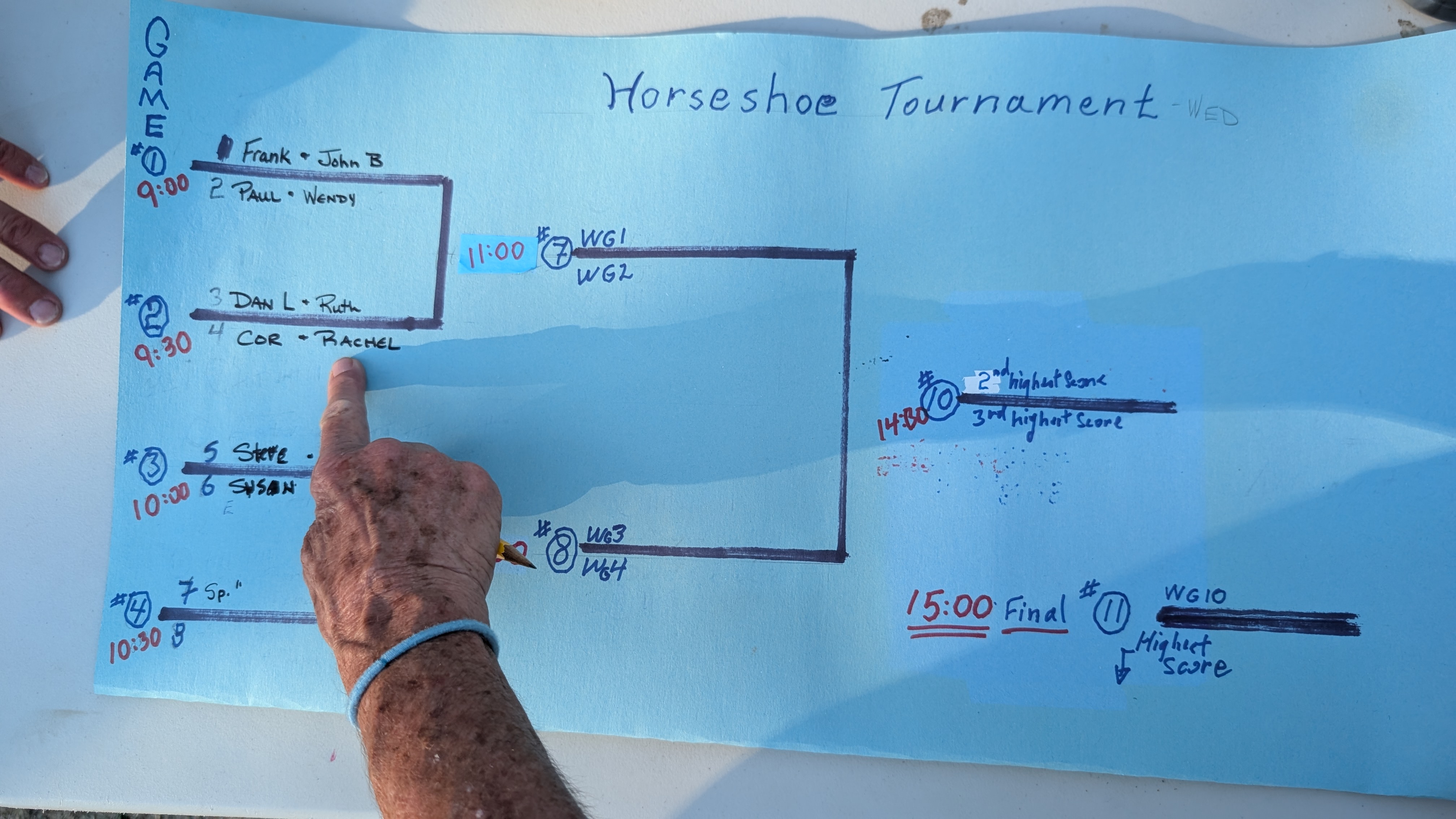 Hand-drawn horseshoe tournament bracket on blue paper showing team pairings and schedule