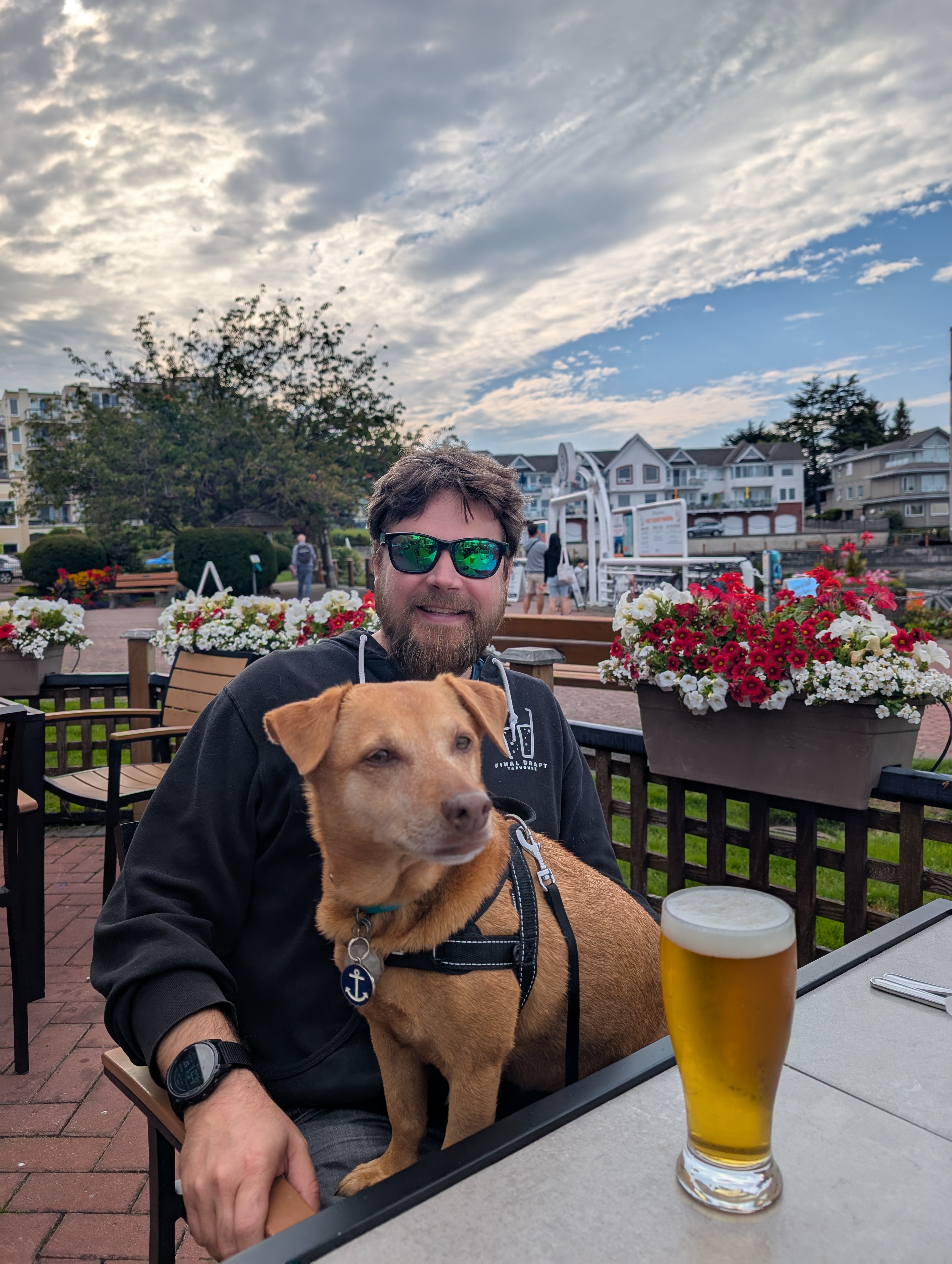 Brian and Maui sitting at a waterfront patio with a pint of beer and flowers in Sidney