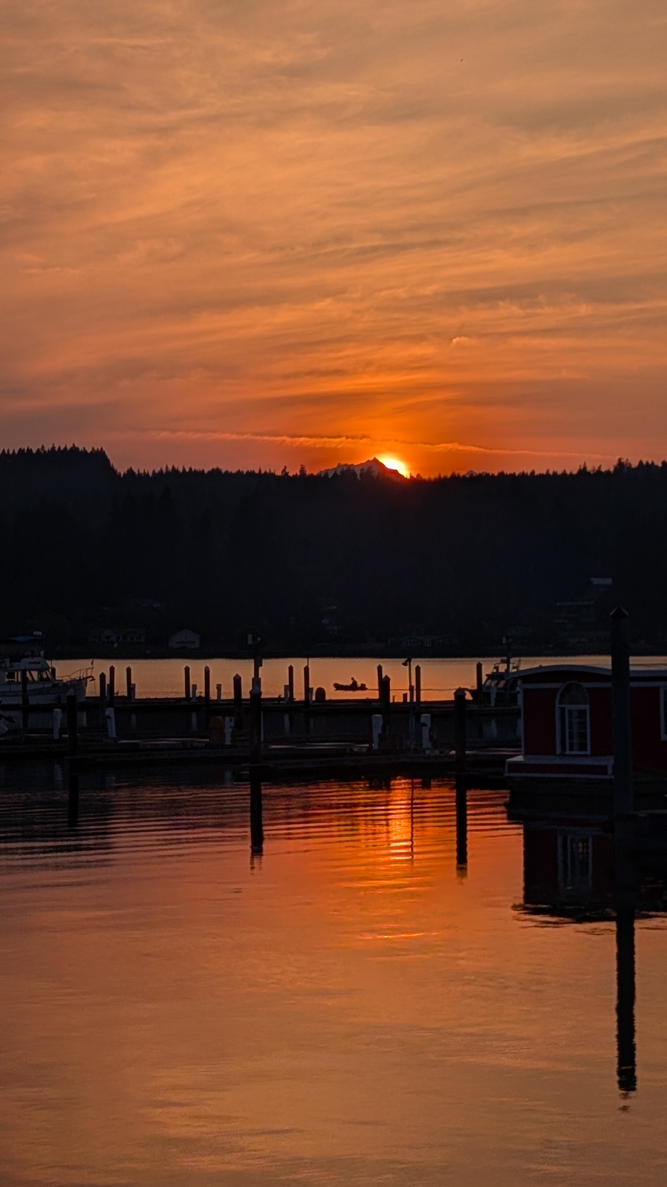 Brilliant orange sunset reflecting in the calm water of Poulsbo harbour with docks and boats silhouetted