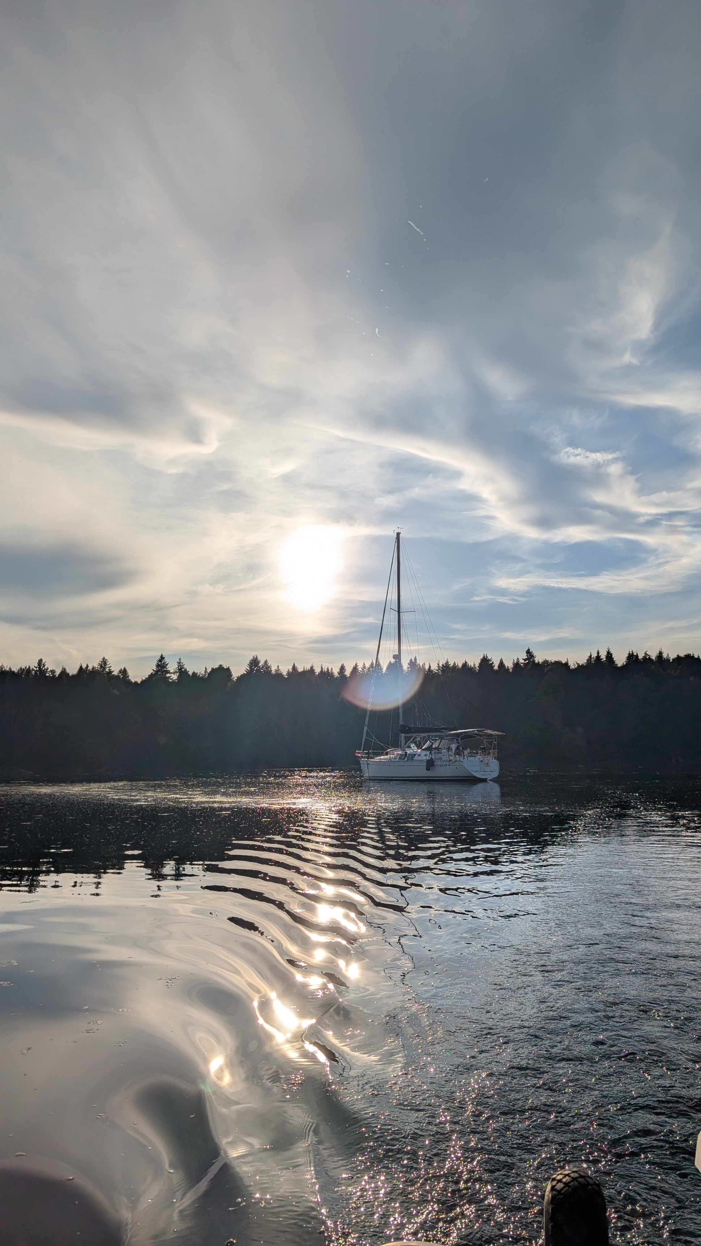 SV Yahara at anchor with sun flare and dinghy wake ripples at McMicken Island